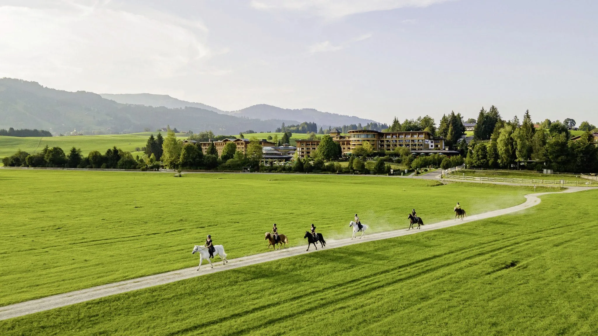 mehrere Reiter bei einem Ausritt in gr&uuml;ner Natur mit dem Sonnenalp Resort und Bergen im Hintergrund
