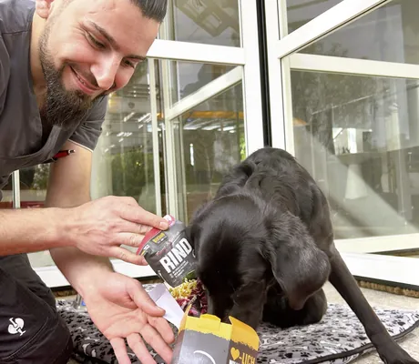 Mann mit Bart gibt schwarzem Hund Leckerli aus der Tüte im Hotel Die Wutzschleife