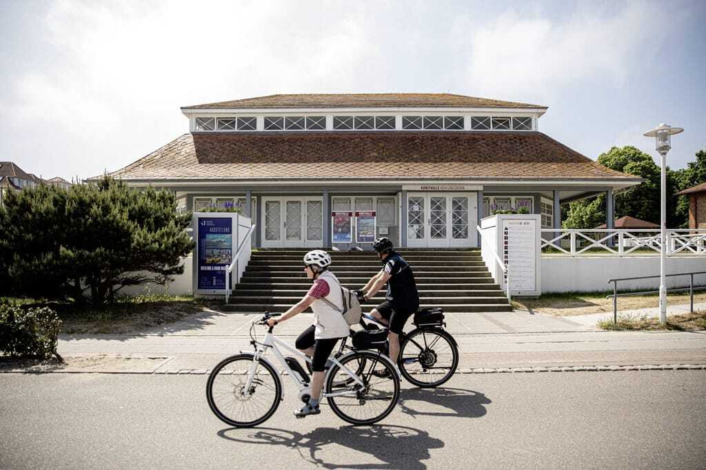 Zwei Radfahrer vor einem historischen Gebäude mit der Aufschrift Kunsthalle Kühlungsborn in der Nähe der Villa Astoria