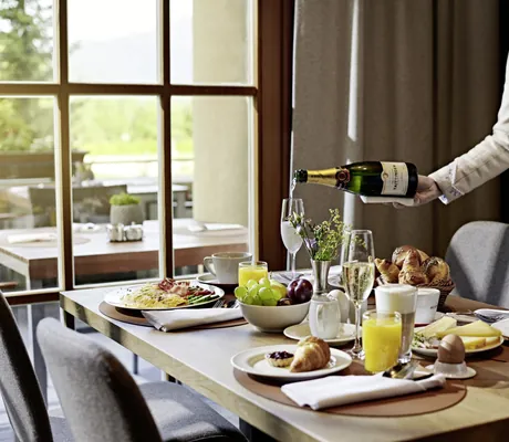 Servicekraft im Dirndl schenkt Champagner am gedeckten Frühstückstisch ein
