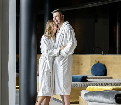 Paar in weißen Bademänteln umarmt sich im Ruheraum des Das Stemp und lacht