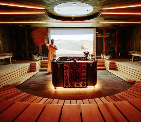 in oranges Gewand gehüllter Mann wedelt mit Handtuch in der Sauna des Mountain Resort Feuerberg