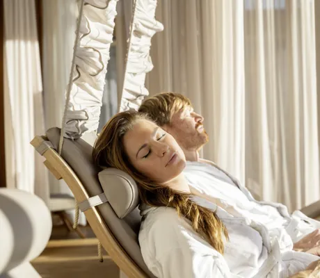 Paar in weißen Bademänteln liegt auf Ruheliegen des Mountain Resort Feuerberg mit Sonne im Gesicht