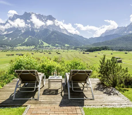zwei Liegestühle auf einer Holzplattform mit Blick auf die Zugspitze im Hotel Post Lermoos