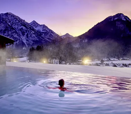 Frau schwimmt in der Abenddämmerung im Outdoorpool des Hotel Prinz-Luitpold-Bad mit Blick auf die Berge