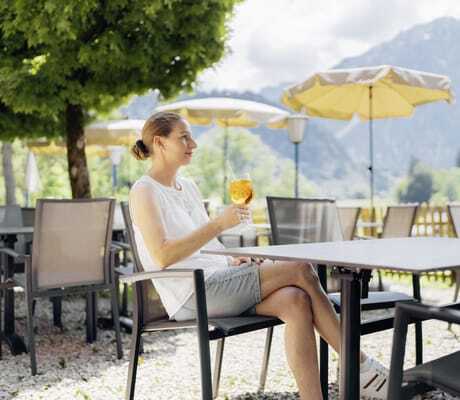 Frau mit Dutt und kurzer Hose sitzt mit Sprizz auf der Terrasse des Hotel Prinz-Luitpold-Bad