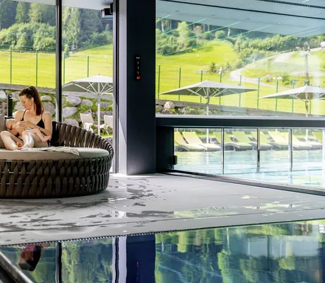 dunkelhaarige Frau stillt Baby auf Liegefläche am Indoorpool in der Riederalm