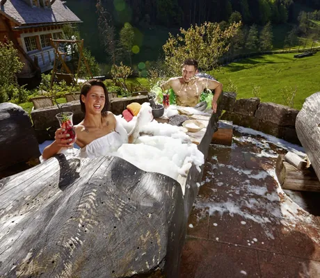 Paar sitzt im Schaumbad in einem Baumstamm im Wellnesshotel Tanne