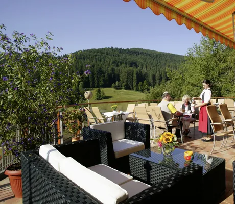 Frau in Tracht bedient Paar auf der Terrasse des Wellnesshotel Tanne