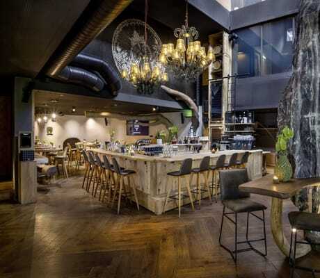 Moderne Bar aus Holz mit Kronleuchtern und dunkelgrauen Barhockern im mama thresl
