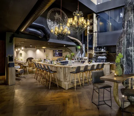 Moderne Bar aus Holz mit Kronleuchtern und dunkelgrauen Barhockern im mama thresl