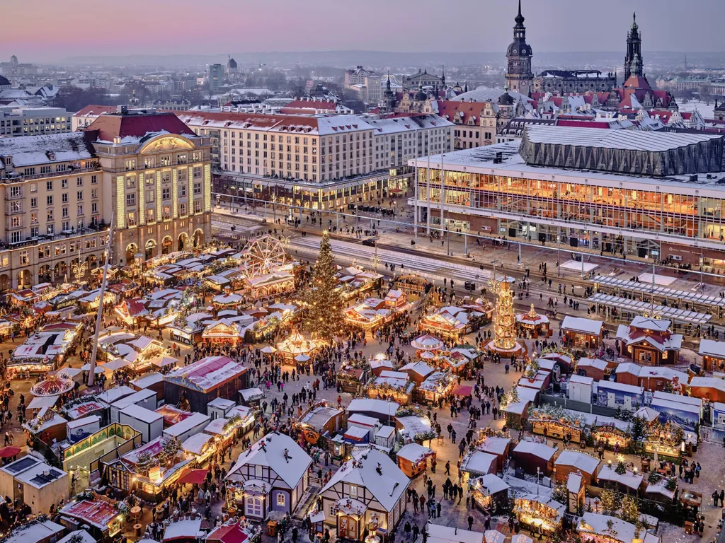 Blick auf den festlich beleuchteten Dresdner Striezelmarkt zur Weihnachtszeit mit Riesenrad, Tannenbaum, Pyramide und Kircht&uuml;rmen im Hintergrund