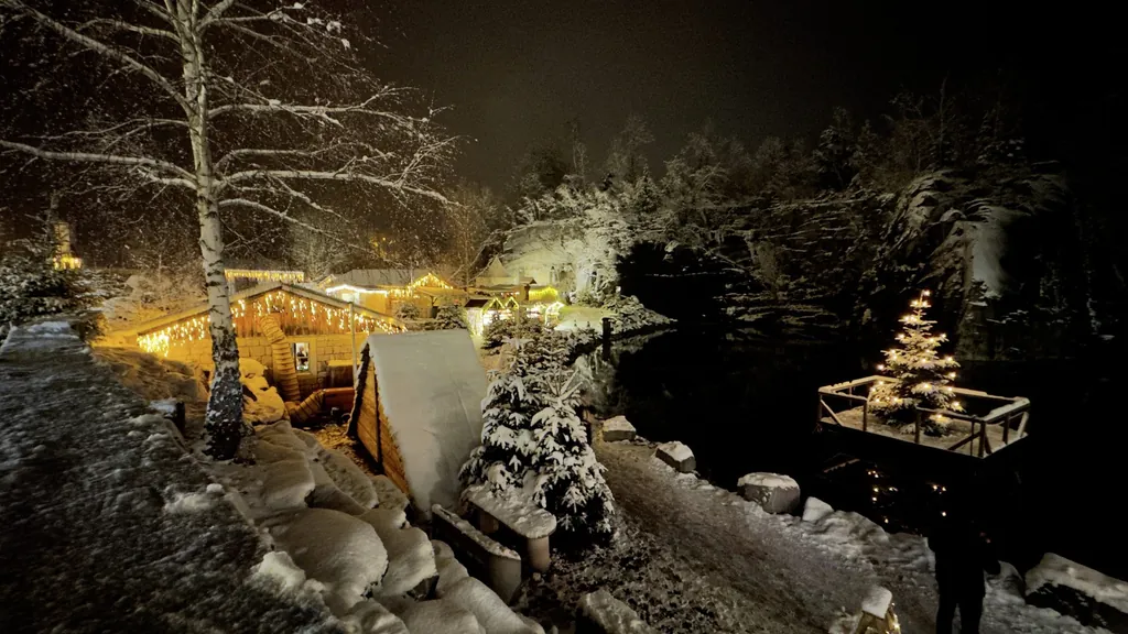 Blick auf den eingeschneiten Weihnachtsmarkt in Hauzenberg mit beleuchteten Marktst&auml;nden und Tannenbaum