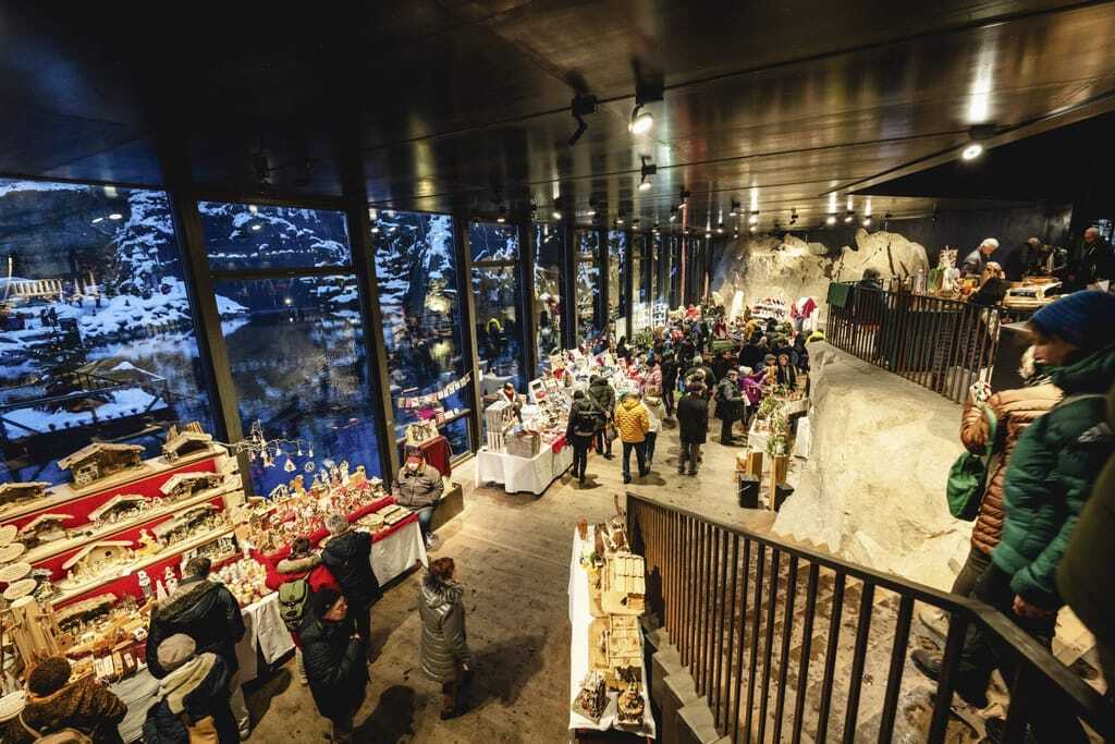 Einige Menschen stöbern an Ständen des weihnachtlichen Indoor-Marktes "Granitweihnacht" mit Blick auf einen See