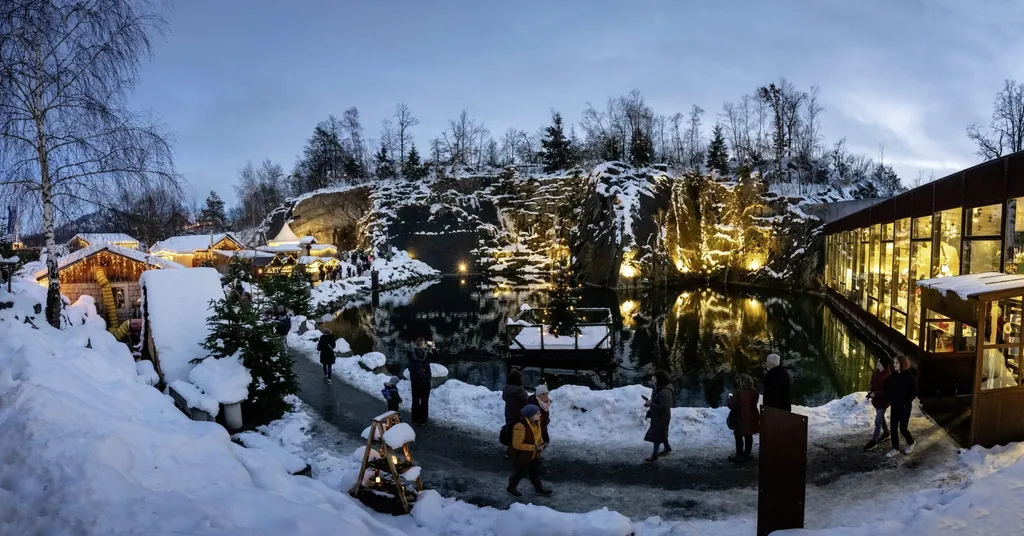Weihnachtlich beleuchtete Holzh&uuml;tten im Schnee und beleuchteter See und Felsw&auml;nde auf dem Weihnachtsmarkt "Granitweihnacht"