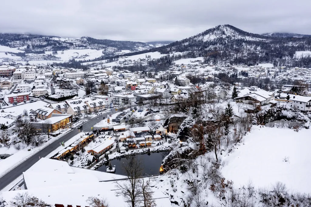 Verschneite Stadtlandschaft mit Bergen und dem Weihnachtsmarkt "Granitweihnacht" im ehemaligen Steinbruch mit kleinem See