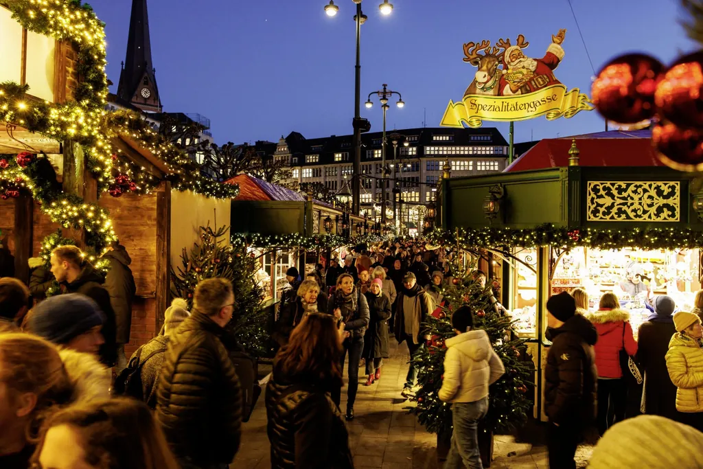 einige Menschen laufen &uuml;ber den Hamburger Weihnachtsmarkt, der festlich beleuchtet ist
