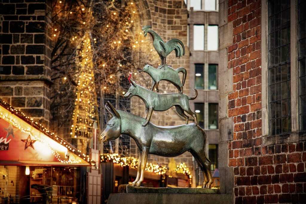 Statue der Bremer Stadtmusikanten mit vier Tieren übereinander Esel, Hund, Katze und Hahn in weihnachtlichem Ambiente mit vielen Lichterketten