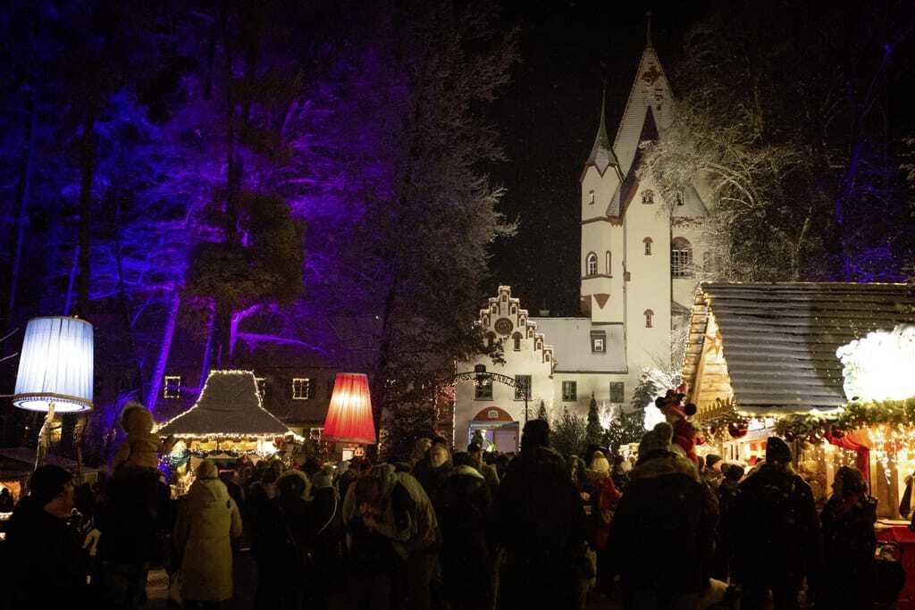 Nachtszene auf dem Weihnachtsmarkt mit beleuchteten Bäumen und Schloss Kaltenberg im Hintergrund