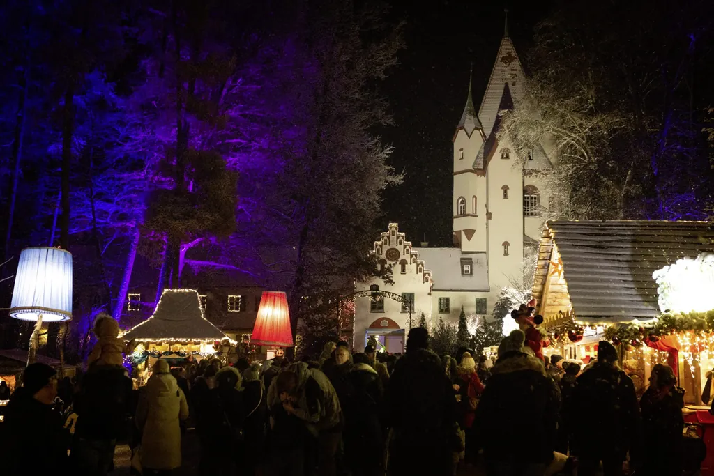 Nachtszene auf dem Weihnachtsmarkt mit beleuchteten B&auml;umen und Schloss Kaltenberg im Hintergrund