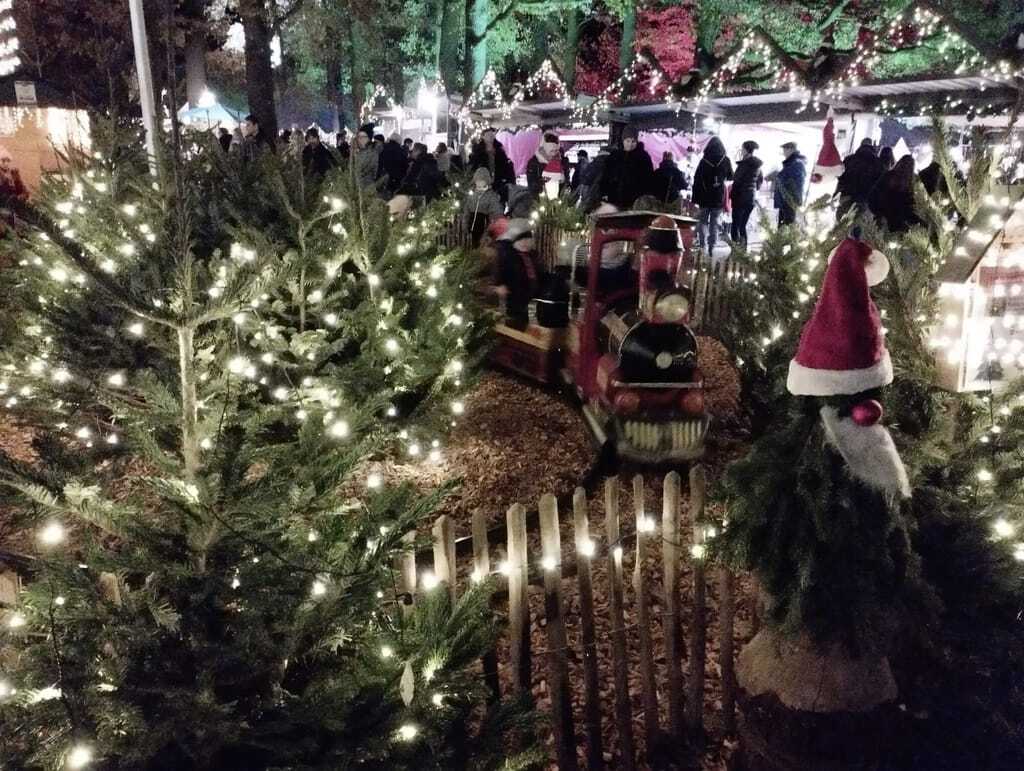 kleine Kindereisenbahn und kleine mit Lichterketten geschmückte Tannenbäume und Weihnachtsmarktstände im Hintergrund