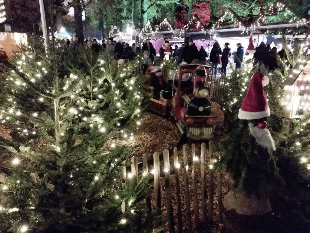 kleine Kindereisenbahn und kleine mit Lichterketten geschm&uuml;ckte Tannenb&auml;ume und Weihnachtsmarktst&auml;nde im Hintergrund
