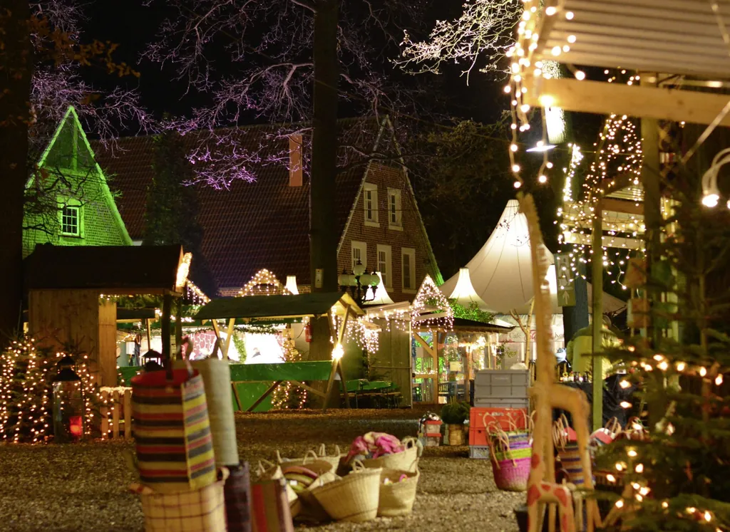 Weihnachtsmarkt auf dem Landgut Krumme mit verschiedenen St&auml;nden, dekoriert mit Lichterketten und beleuchteten H&auml;usern im Hintergrund