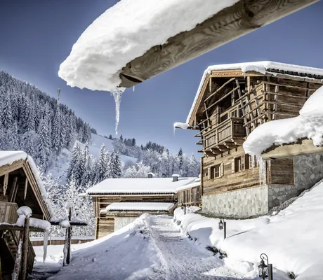 Verschneite Chalethütten des Bergdorf Prechtlgut in alpiner Winterlandschaft mit strahlend blauem Himmel