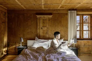 dunkelhäutige Frau liest im Bett des holzgetäfelten Zimmers Zeitung