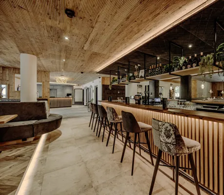 Blick in die moderne Bar des Familienresort Reslwirt mit Holzdekor, einigen Pflanzen und stilvollen, gepolsterten Barhockern