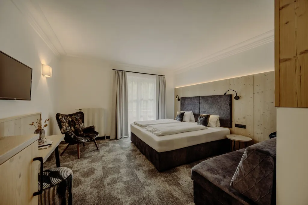Blick in ein Zimmer des Familienresort Reslwirt in Grautönen mit Holzdetails und großem Doppelbett, gemütlichem Sessel, TV und gepolsteter Sitzbank