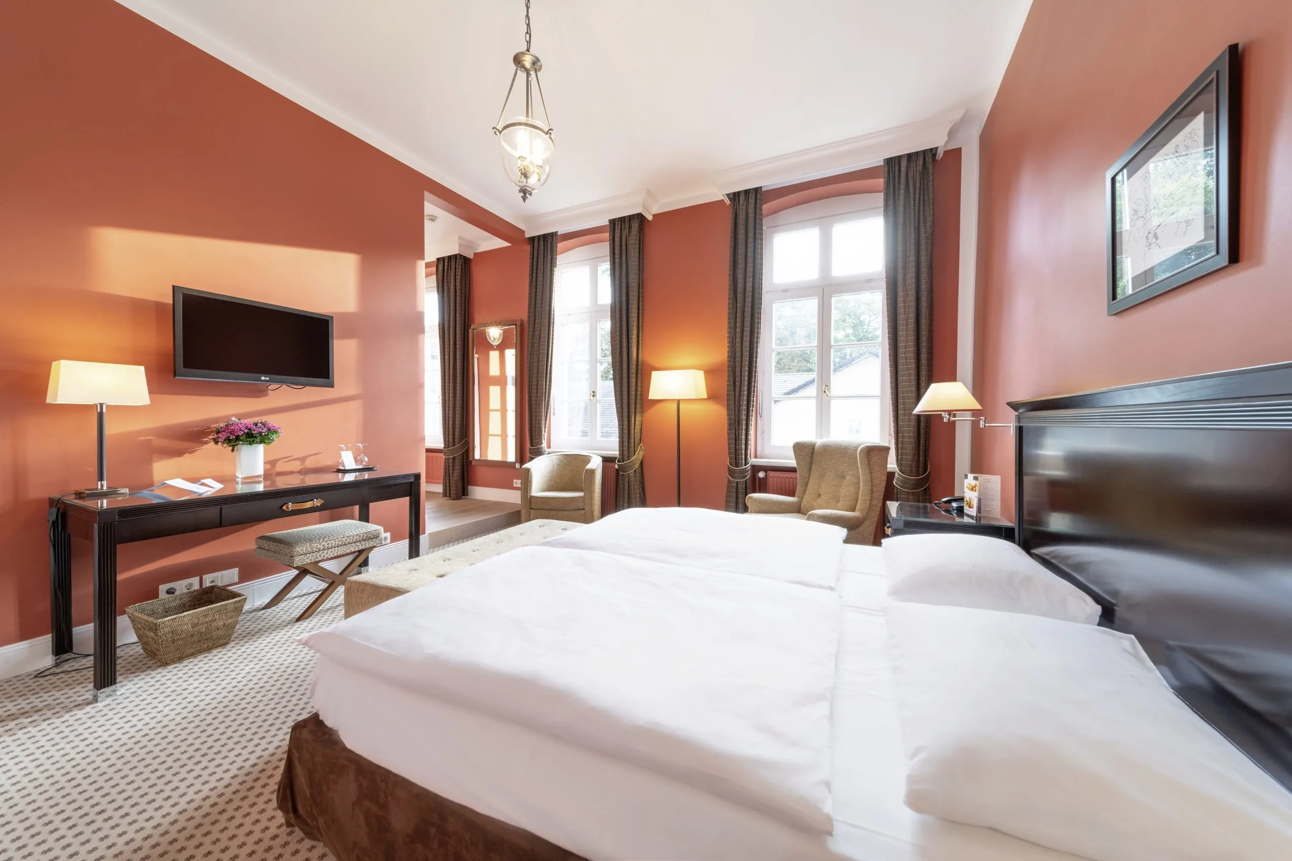 Hellrote W&auml;nde, zwei gem&uuml;tliche Sessel vor den wei&szlig;en gro&szlig;en Fenster und schwarze M&ouml;bel.