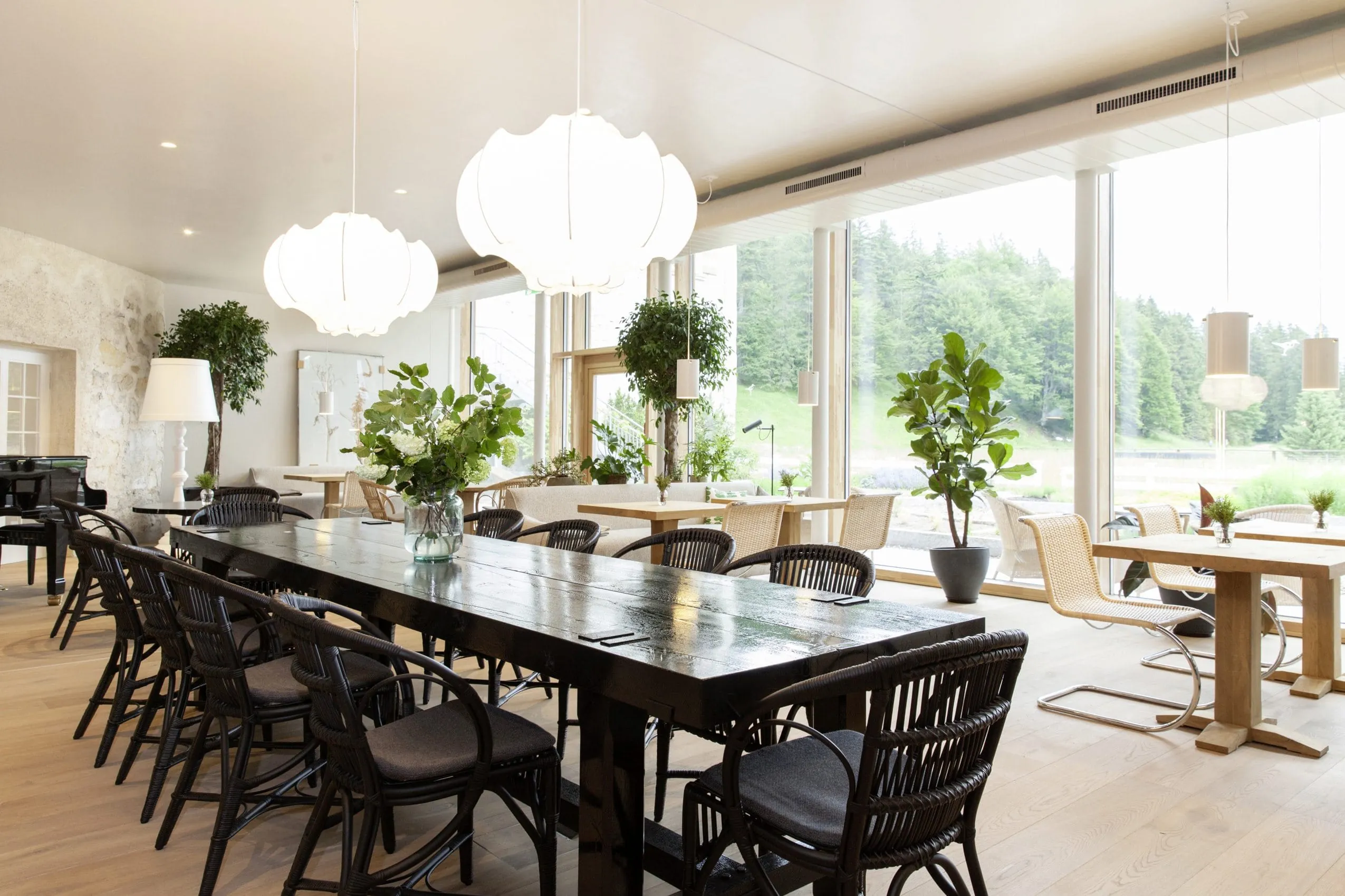 Restaurant mit gro&szlig;er Tafel in dunkelbraunem Holz als Eyecatcher in der Mitte. Au&szlig;enrum helle Einzeltische f&uuml;r zwei bis vier Personen