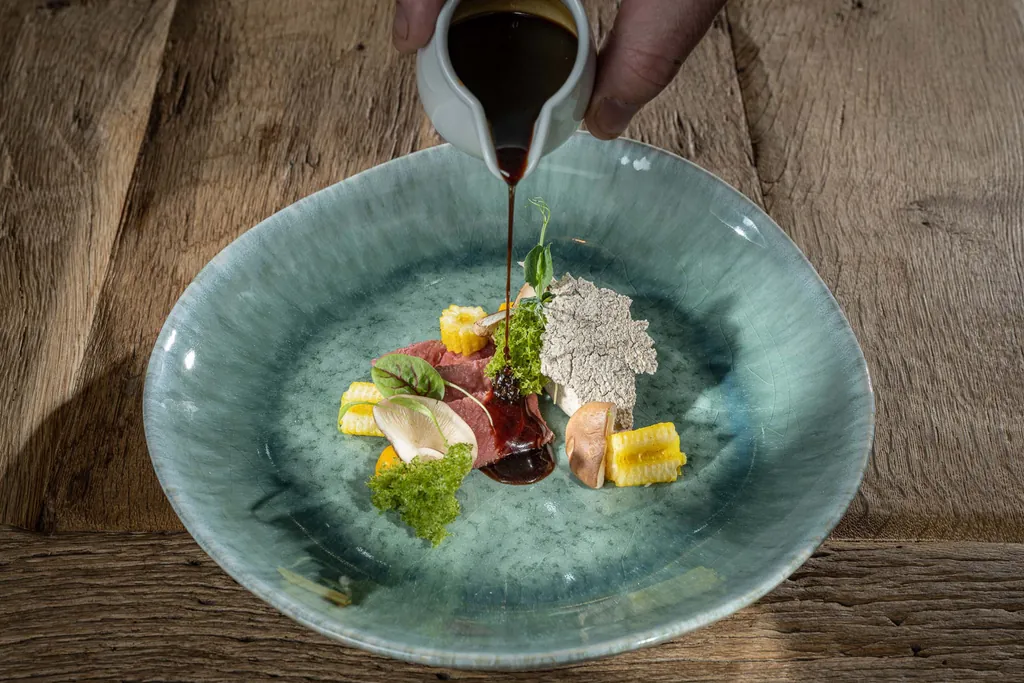 Blau-t&uuml;rkis handglasiertes Teller auf dem eine Komposition aus Fleisch und regionalem Gem&uuml;se angerichtet sind.