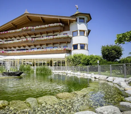 Außenaufnahme Gartenhotel Magdalena mit Geranienkästen an den Balkonen und Naturteich vor der Terrasse