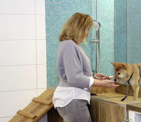 blonde Frau steht am Hundewaschplatz mit Dusche des Gartenhotel Magdalena und wäscht ihren Hund