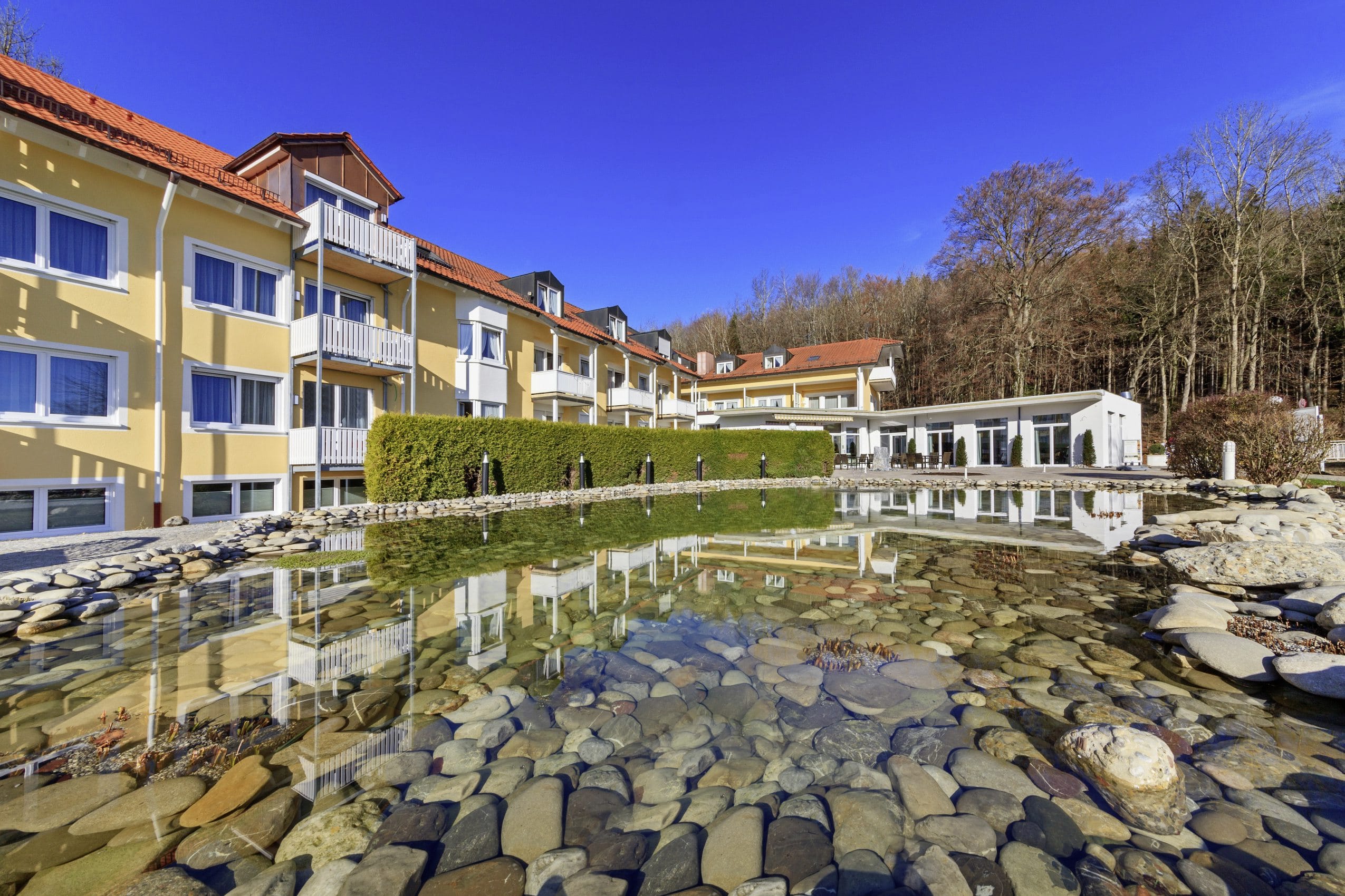 Blick über den Naturteich auf die Fassade des Vitalhotel Sonneck mit weißen Balkonen