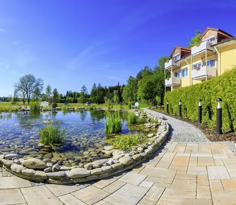 Naturbadeteich vor der Fassade des Vitalhotel Sonneck im Sommer mit Gräsern