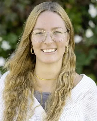 Autorenporträt Lena Schmidberger mit runder Brille, langen, welligen Haaren und weißer Strickjacke