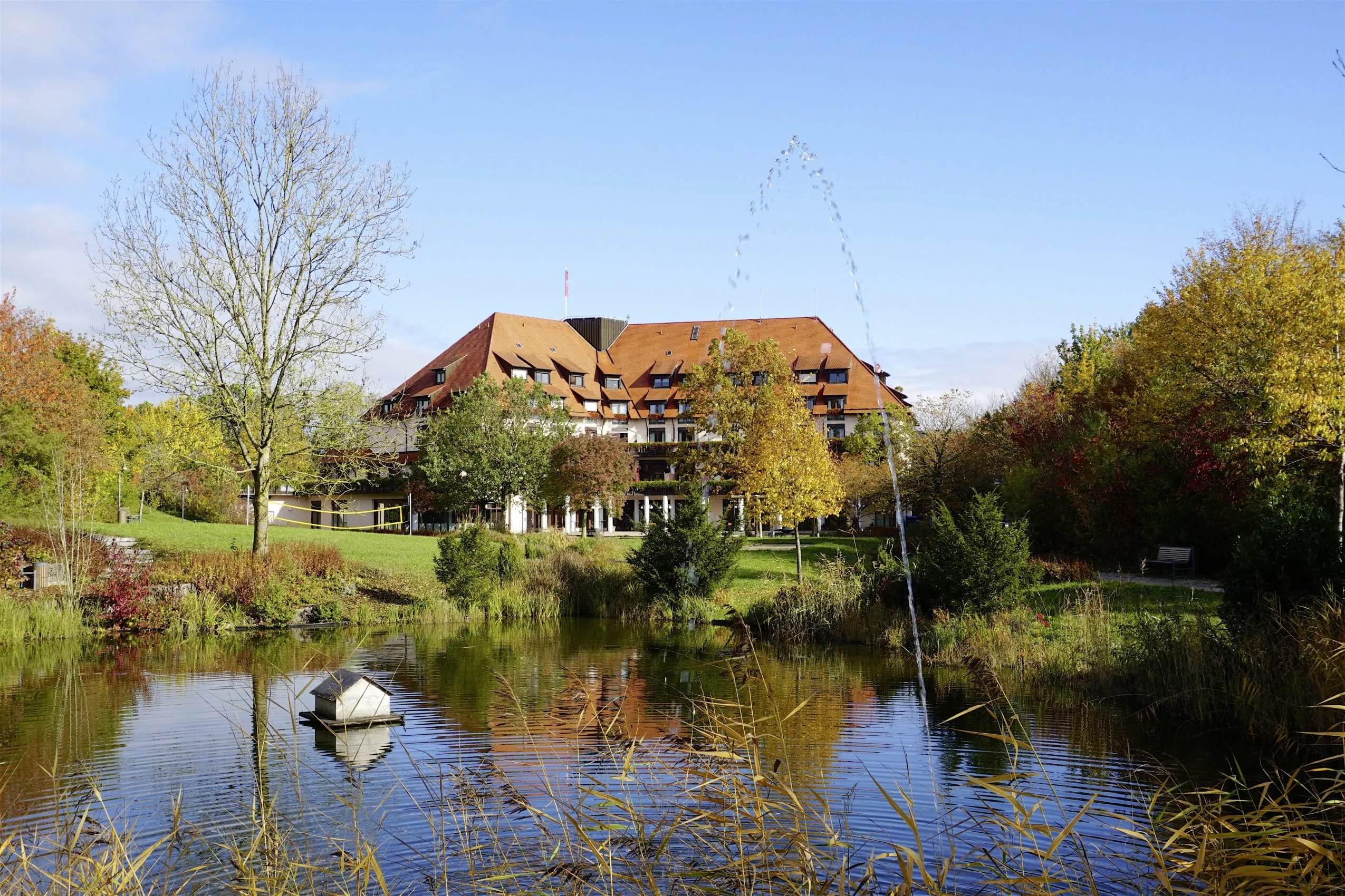Gesamtansicht des Flair Park-Hotel Ilshofen mit Naturteich in herbstlicher Landschaft