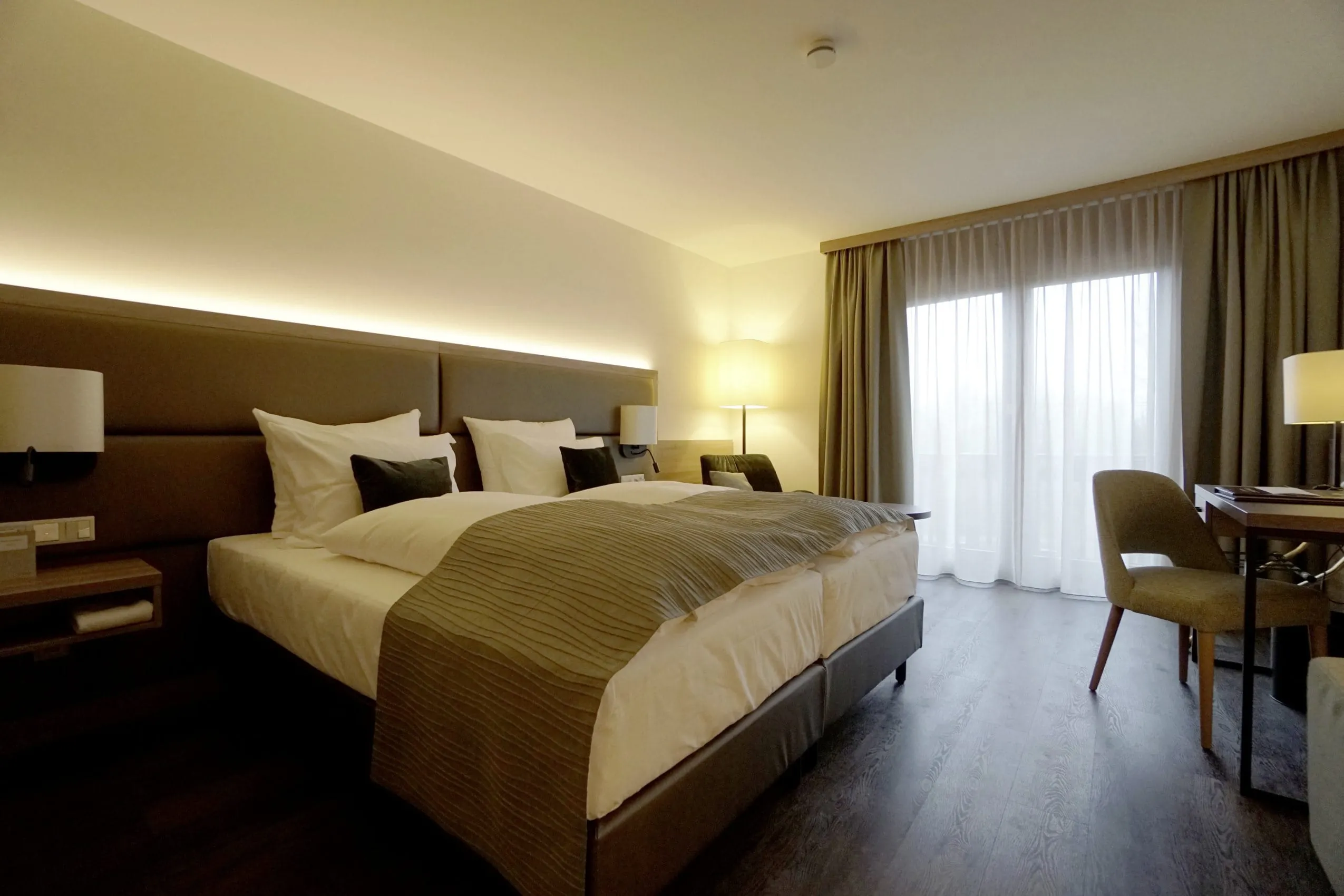 Zimmer im Flair Park-Hotel Ilshofen mit beigem Bett&uuml;berwurf und Stoff-R&uuml;ckwand