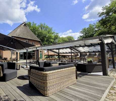 Terrasse in Gut Thansen mit Korbmöbeln und dunklen Polstern neben reetgedeckter Scheune