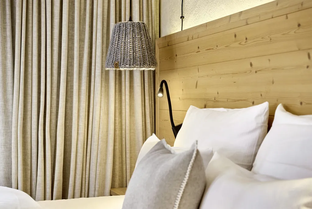 Boxspringbett mit Kopfteil aus Holz, vielen Kissen und Lampe mit Wollbezug