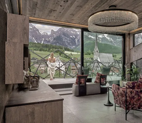 Frau mit Stola steht auf Balkon vor Wellness-Lounge mit großem runden Kronleuchter im die Hochkönigin