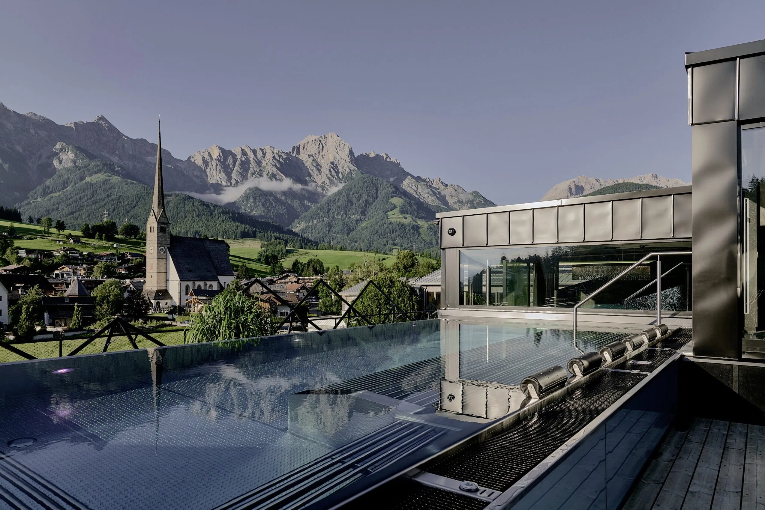 Outdoorpool mit Whirlliegen und Blick auf die Kirche von Maria Alm im die Hochkönigin