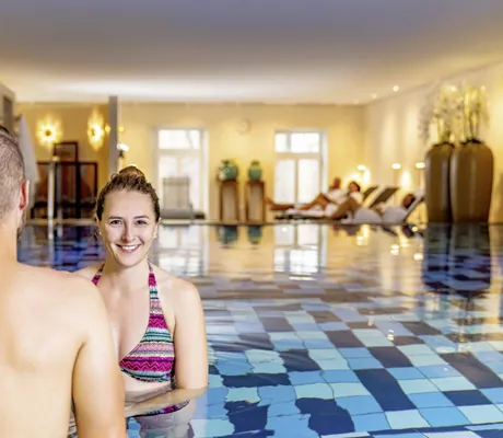 Frau mit buntem Bikini im Indoorpool des Jugendstilhotel Bellevue lacht in die Kamera