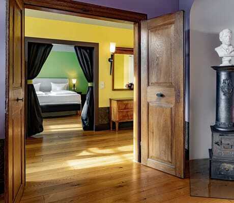 Suite im Jugendstilhotel Bellevue mit Schlafzimmer hinter grünem Vorhang und altem Ofen mit Büste im Vordergrund