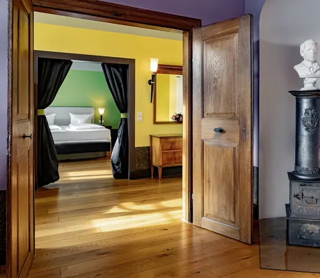 Suite im Jugendstilhotel Bellevue mit Schlafzimmer hinter grünem Vorhang und altem Ofen mit Büste im Vordergrund