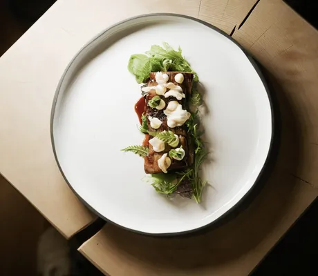 Fleischgericht mit Salat auf weißem Teller auf Holz im Hotel Pfösl