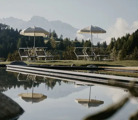 zwei Sonnenplätze mit Schirmen und Liegestühlen am Beckenrand des Hotel Pfösl mit Blick auf die Dolomiten